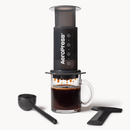 Cafetera AeroPress Original sobre una taza de vidrio con cuchara medidora y agitador