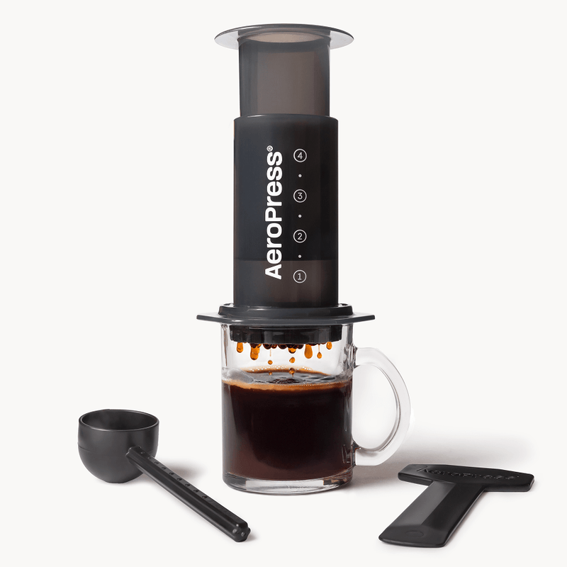 Cafetera AeroPress Original sobre una taza de vidrio con cuchara medidora y agitador