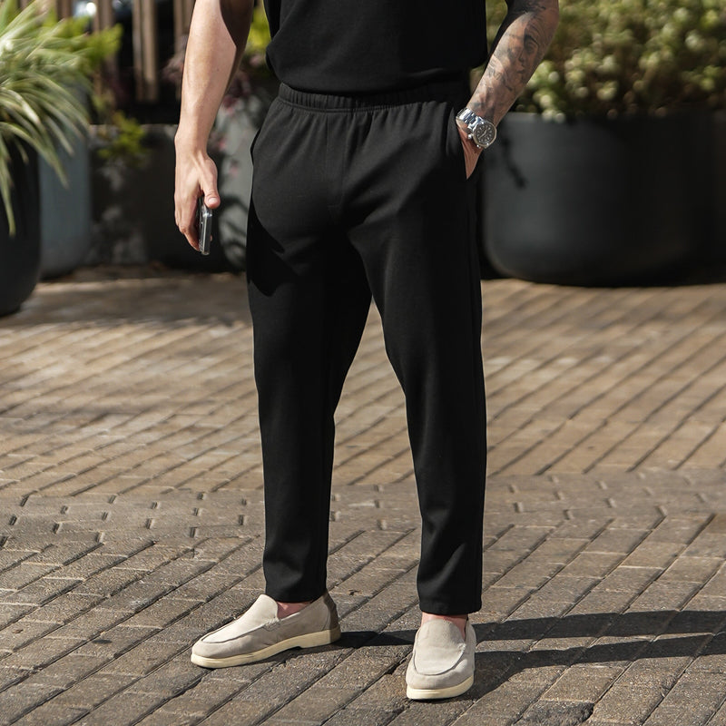 Hombre usando Casual Chinos V2 negros al aire libre en un camino pavimentado