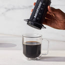 Mano levantando una AeroPress sobre una taza de café preparado