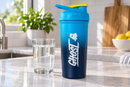 Coctelera azul GHOST de pie sobre una luminosa encimera de cocina junto a un vaso de agua