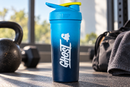 Coctelera azul GHOST junto a pesas de gimnasio y una bolsa de entrenamiento negra