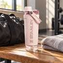 Botella rosa Vitalize sobre una mesa de madera junto a una bolsa de gimnasia y una toalla