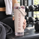 Mano sosteniendo la botella rosa Vitalize junto al equipo de gimnasio