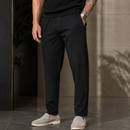 Hombre usando chinos negros y zapatos blancos frente a un fondo de piedra