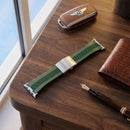 Correa verde GT WING con broche metálico sobre una mesa de madera