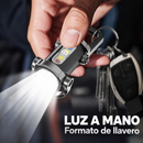 Mano sosteniendo una linterna en formato de llavero con luz frontal encendida, junto a un juego de llaves.