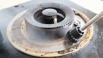 Boquilla de un limpiador de vapor portátil dirigida hacia una hornilla sucia de una estufa de gas